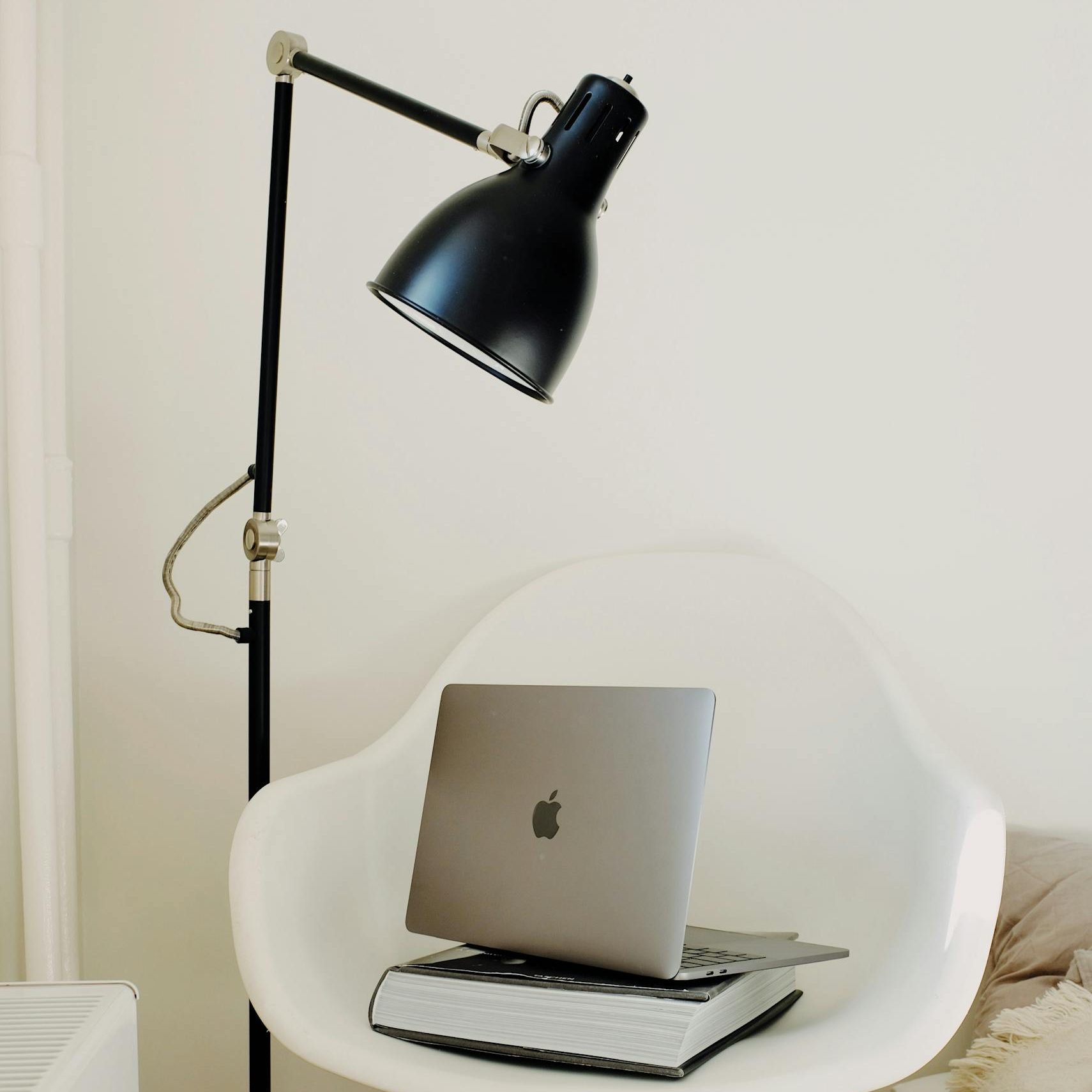 A cozy, modern workspace featuring a laptop on a chair, next to a stylish lamp, embodying minimalism.