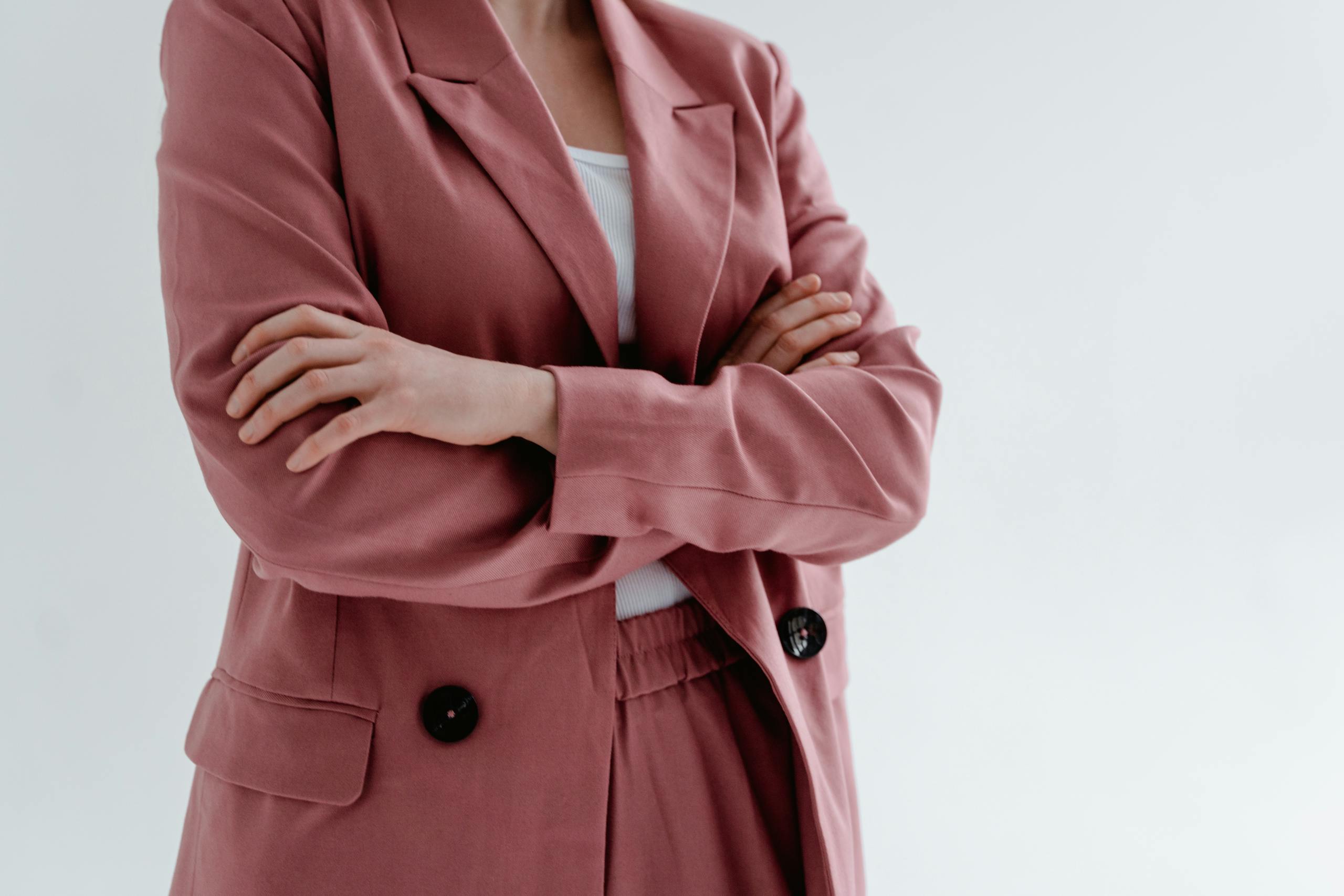 Close-up of a woman in a pink blazer with arms crossed, conveying confidence.